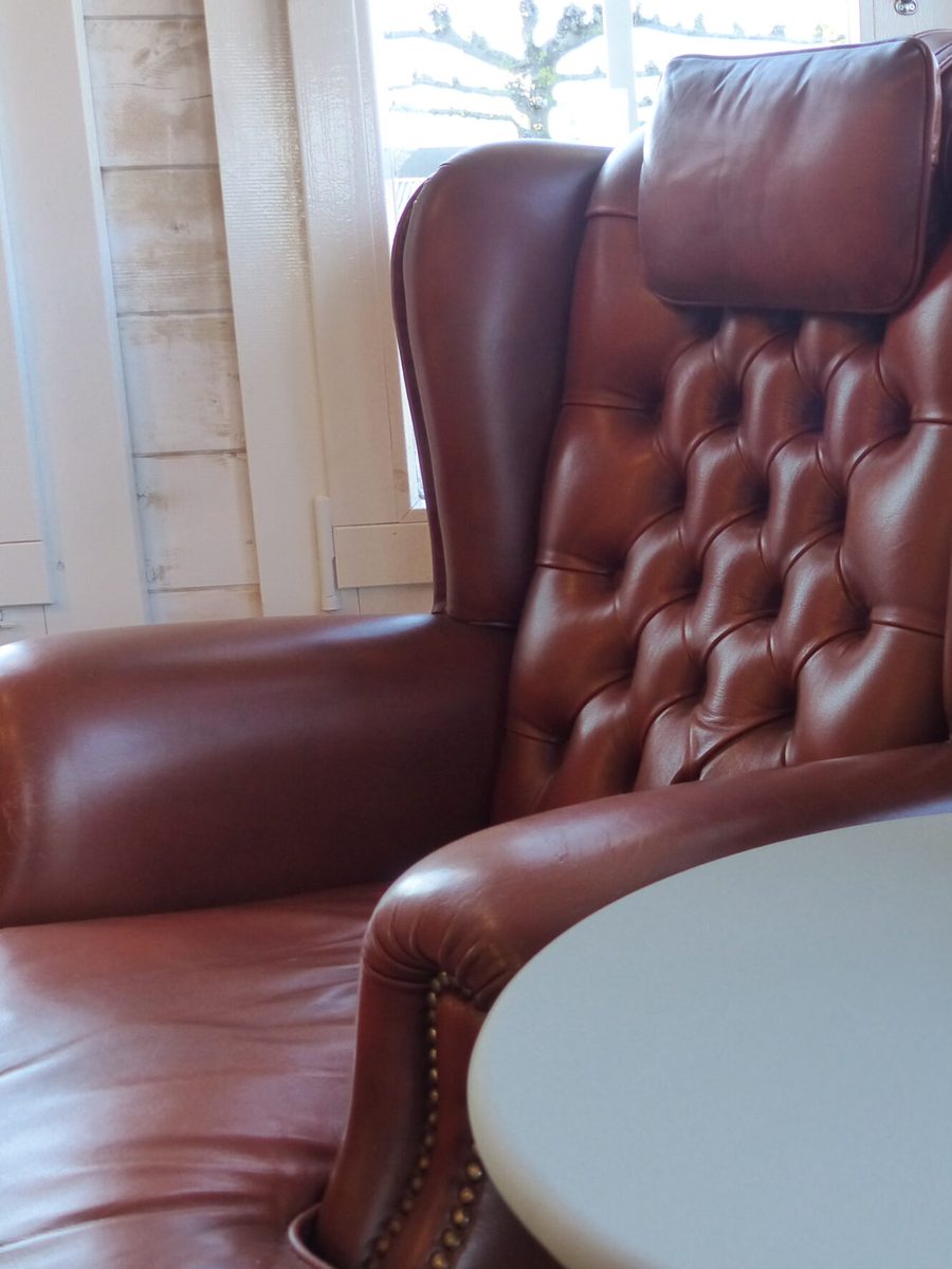 De leren oorfauteuil met knoopstiksels in de salon